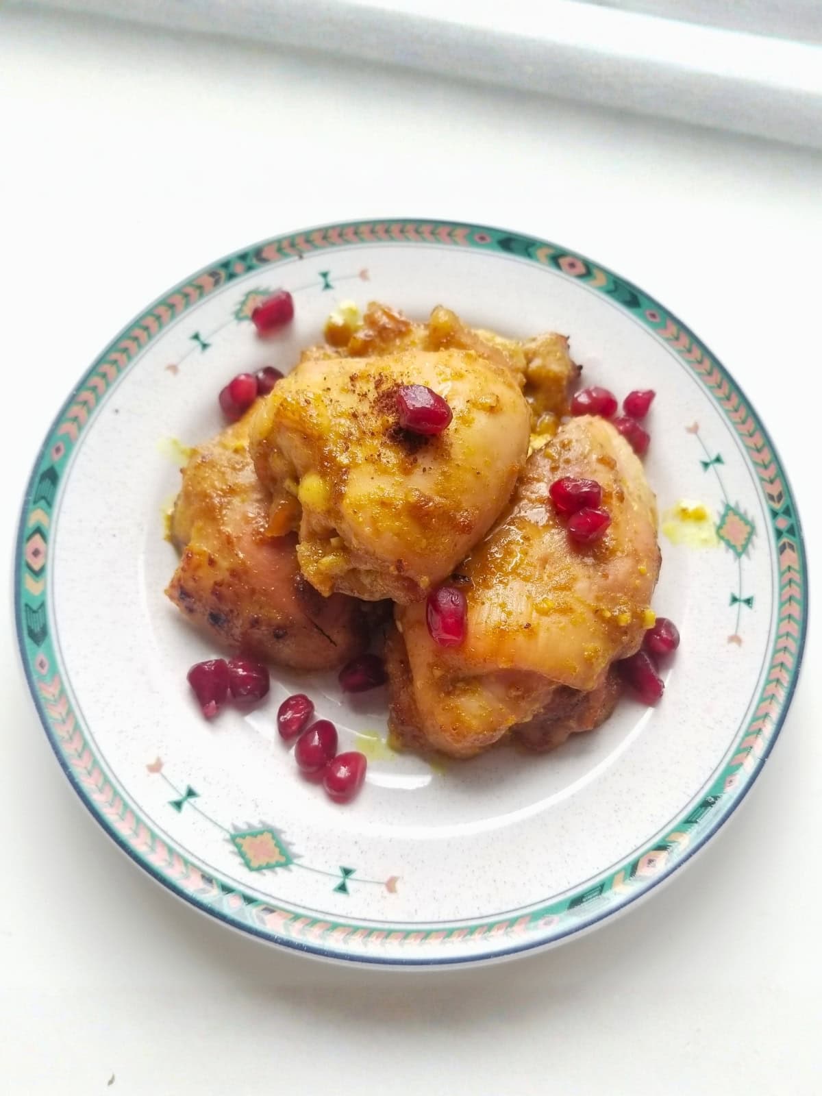 Cooked honey turmeric chicken thighs on a plate, topped with pomegranate seeds.