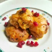 Cooked honey turmeric chicken thighs on a plate, topped with pomegranate seeds.