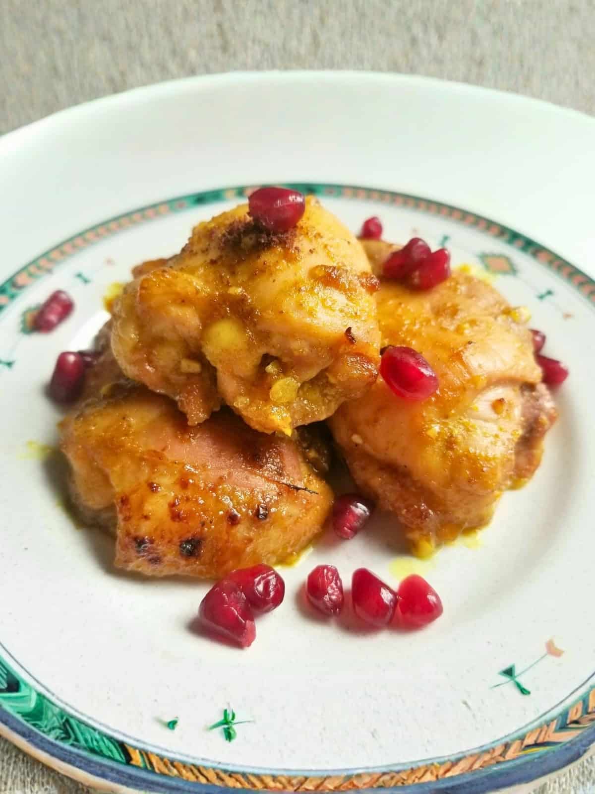 Cooked honey turmeric chicken thighs on a plate, topped with pomegranate seeds.