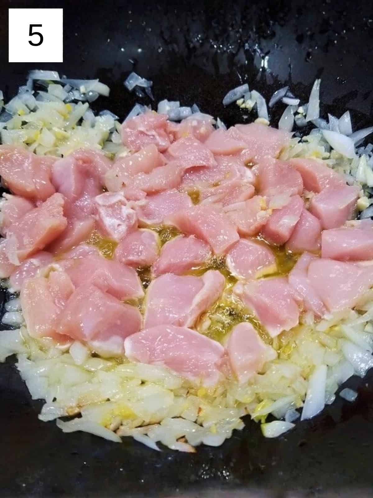 Chopped chicken breast in a pan with a mixture of sauteed spices.