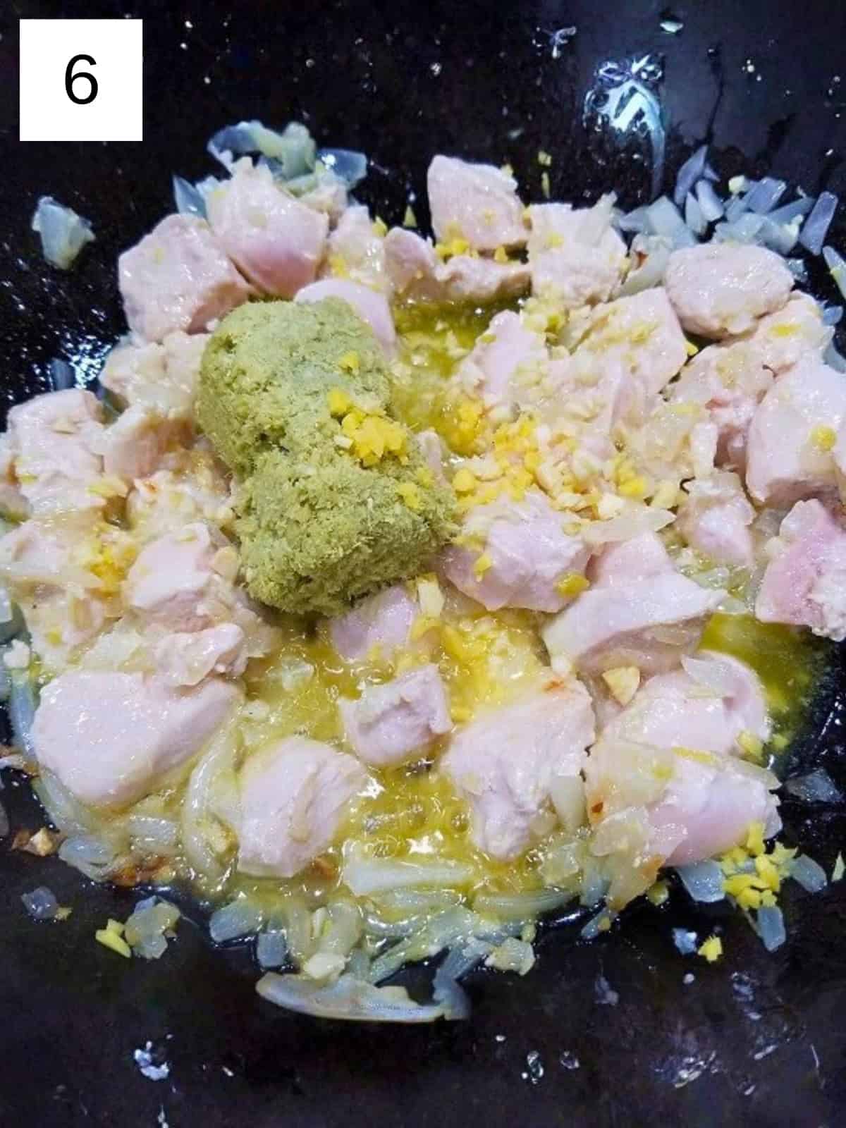 Half-cooked chicken pieces with minced garlic and ginger in a pan, along with a sauteed spices.