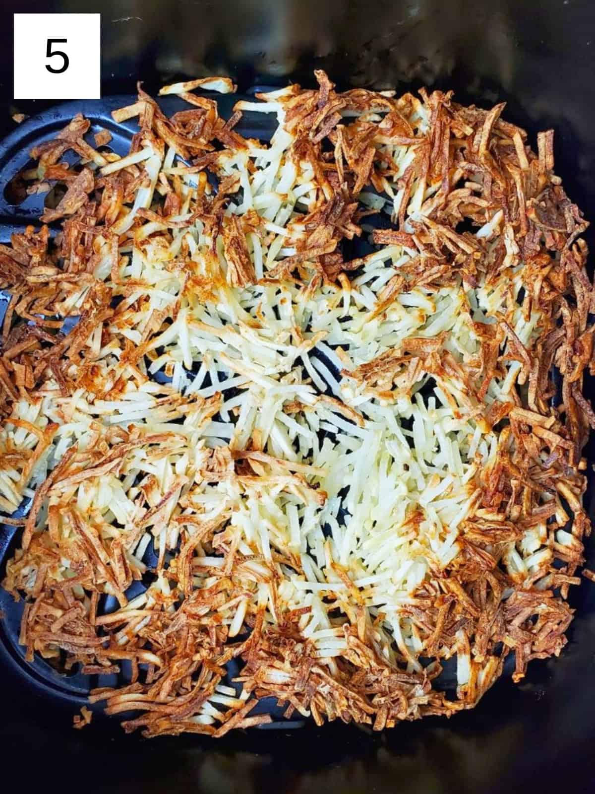 Cooked shredded hashbrowns inside an air fryer.