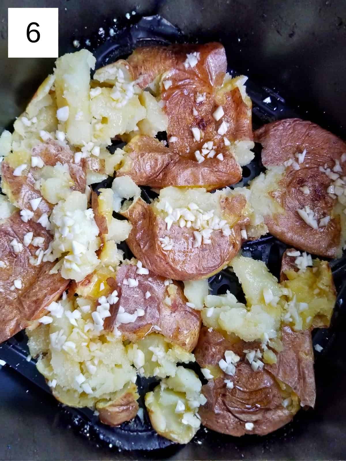 Smashed potatoes in an air fryer basket, sprinkled with salt and minced garlic.