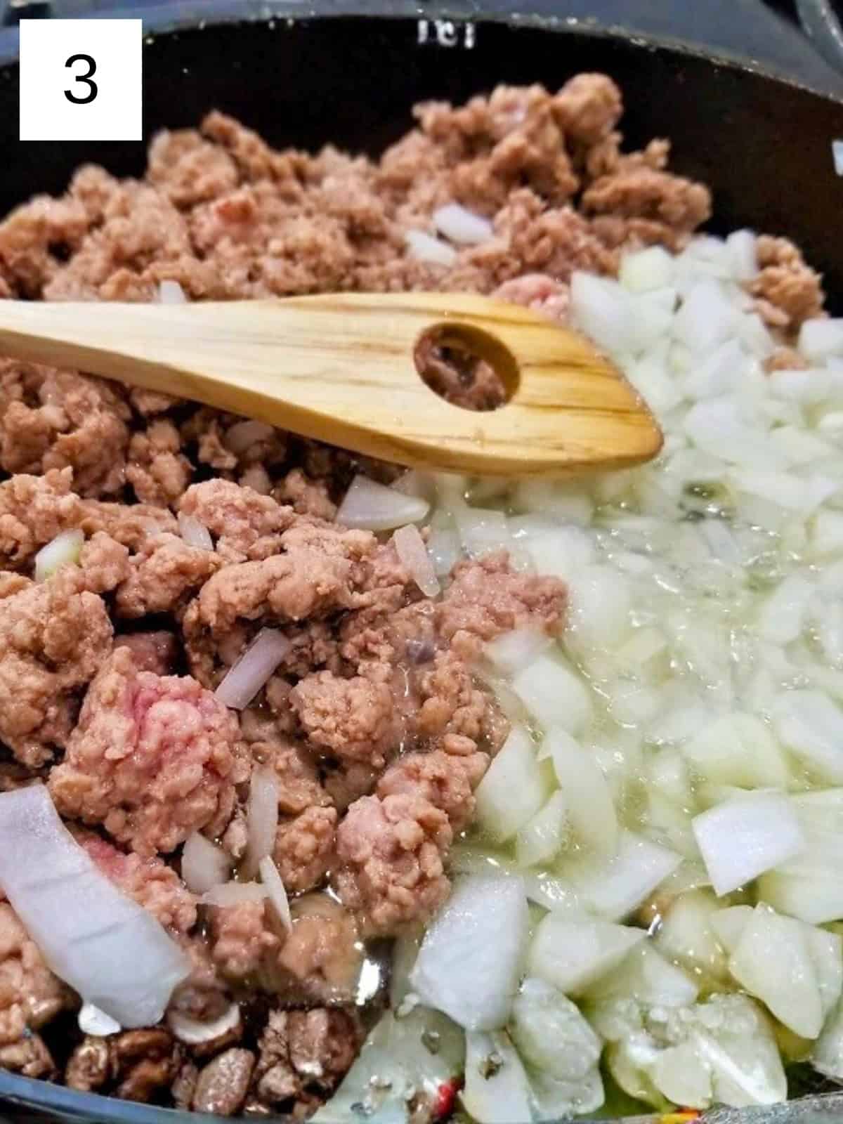 Half cooked ground chicken and sliced onion in a cast iron pan.