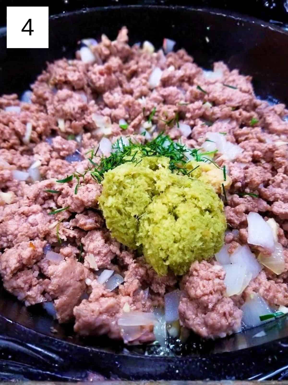 A mixture of ground chicken, onion, ginger, lemongrass, garlic, and chopped lime leaves, in a cast iron pan.